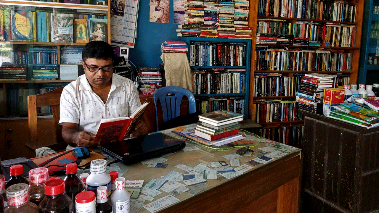 নিজের দোকানে বসে বই পড়ছেন বিজয়