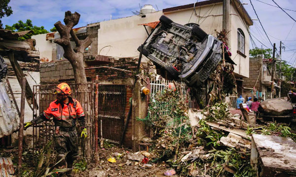 মেক্সিকোর পোজা রিকায় একটি ক্ষতিগ্রস্ত বাড়ির বেড়ার ওপর ঝুলন্ত গাড়ির কাছে কাজ করছেন টোপোস নামে পরিচিত স্বেচ্ছাসেবক দলের একজন উদ্ধারকর্মী : ইন্টারনেট